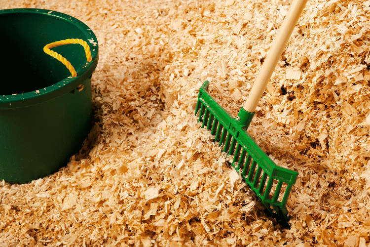 A pile of bulk wood shavings for the worm bedding with manure fork and green bucket