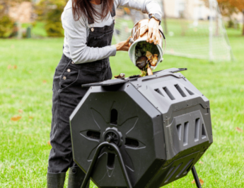 A woman dumping a small bin of kitchen scraps into an outdoor compost tumbler